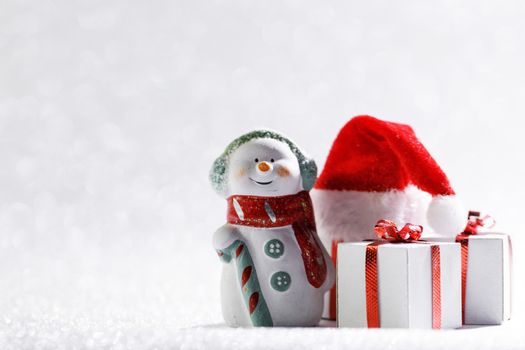 Christmas snowman with gifts and santa claus hat on bright bokeh background