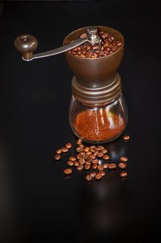 Hand operated coffee grinder with roasted beans on a black background.