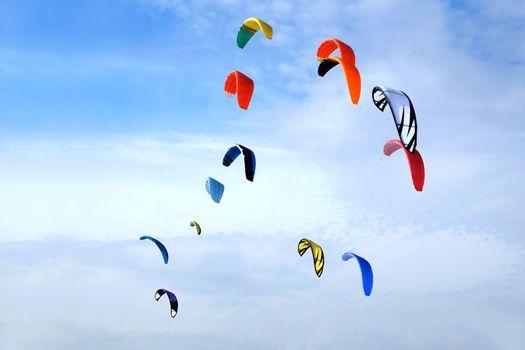 Many big colorful sport kites flying high in bright blue sky on sunny day