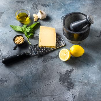 Green basil pesto italian recipe ingredients . Parmesan cheese, basil leaves, pine nuts, olive oil, garlic, salt, pepper and mortar. on gray concrete scratches stone background space for text.