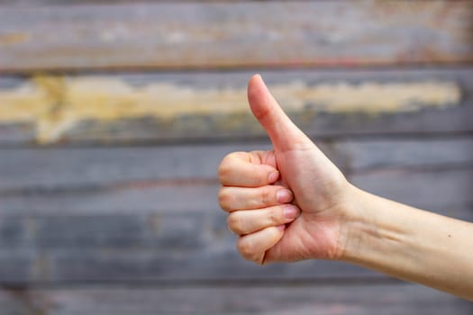 A girl or woman shows a thumbs up, class, on a wooden background. Recommends