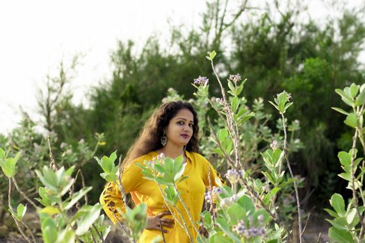 A beautiful Asian woman is standing near the Aak, Madar (Calotropis gigantea) tree wearing a yellow top and selective focus points background,outdoors portrait