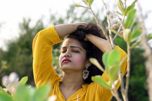 A beautiful Asian woman is standing near the tree of Aak, Madar (Calotropis gigantea) wearing a yellow top and holding black and long hair in her hands, elective focus points background,outdoors