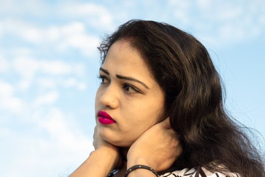 Close up photo shot of an Indian model with beautiful face with blurred background of sky with white clouds and looking away