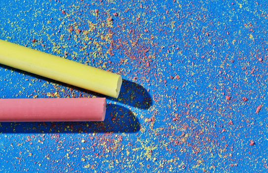Yellow and red thick stick of chalk on blue background , small pieces of yellow and red chalk scattered on the background