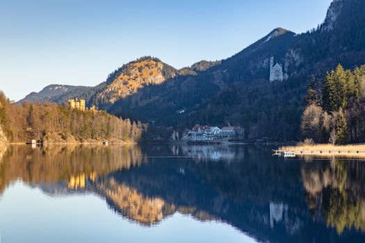 Stunning view of the Alpsee lake in winter on a sunny day with the Neuschwanstein Castle, Hohenschwangau Castle and Bavaria Alps in background, with beautiful reflections in water, Schwangau, Bavaria, Germany