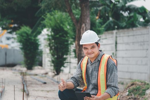 Asian man civil construction engineer worker or architect with helmet and safety vest working and holding a touchless tablet computer for see blueprints or plan at a building or construction site