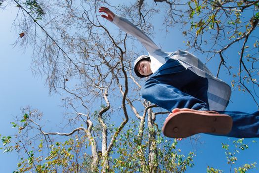 Low angle view of woman midair by jumping, crossing step over the camera shot below in forest with tree and sky overhead in concept travel, active lifestyle, overcome obstacles in life or future