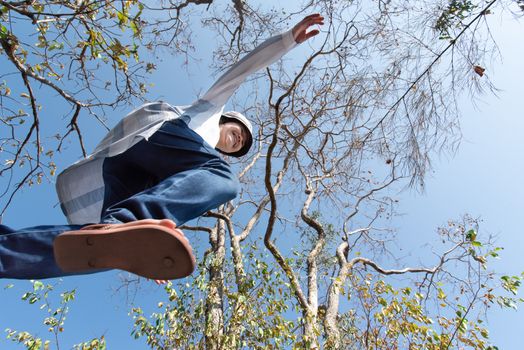 Low angle view of woman midair by jumping, crossing step over the camera shot below in forest with tree and sky overhead in concept travel, active lifestyle, overcome obstacles in life or future