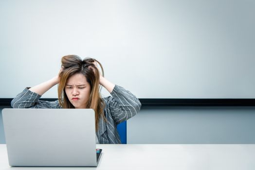 Asian woman is student,businesswoman working by computer notebook, laptop in office meeting room with whiteboard background with annoyed, displeased emotion in concept working woman,unhappy in life