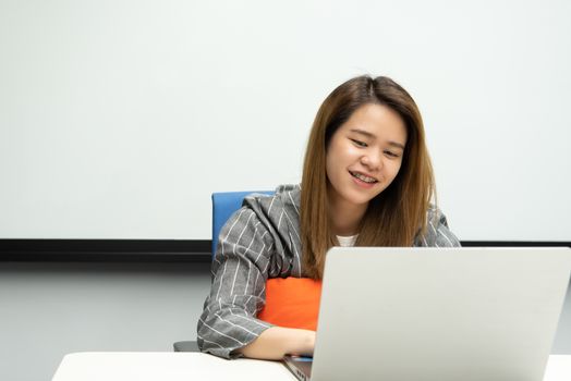 Asian woman is student, businesswoman working by computer notebook, laptop in office meeting room with whiteboard in background with happy and relax emotion in concept working woman, success in life