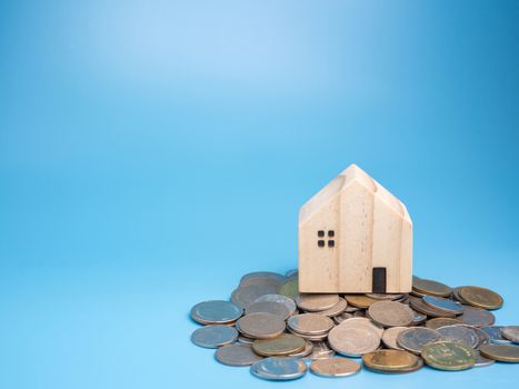 A model wooden house and a pile of coins On a blue background.