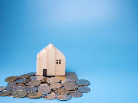 A model wooden house and a pile of coins On a blue background.