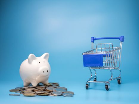 A shopping cart With a pile of coins and Piggy bank  On a blue background. Mortgage concept. Money and house. Financial status.