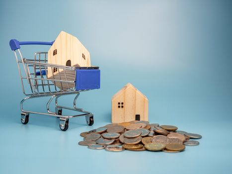 A model wooden house on a shopping cart With a pile of coins On a blue background. Mortgage concept. Money and house.