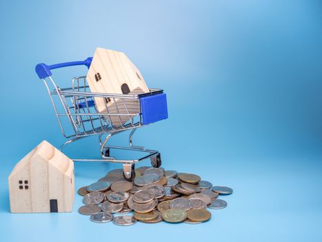 A model wooden house on a shopping cart With a pile of coins On a blue background. Mortgage concept. Money and house.