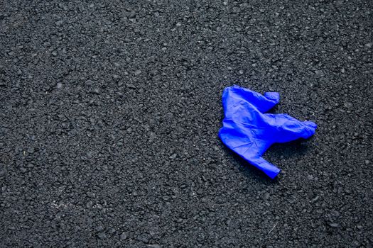 A Used Blue Medical Glove On a Blacktop Road To Protect From Coronavirus