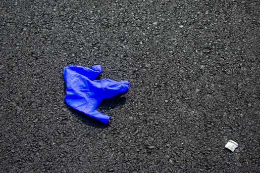 A Used Blue Medical Glove On a Blacktop Road To Protect From Coronavirus