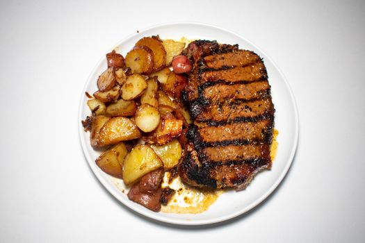 A Perfectly Grilled Steak With Black Grill Lines and Potatoes Plated on a Pure White Background