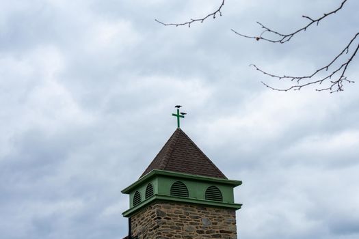 The Tower of a Cobblestone Church With a Cross on Top on a Cloudy Overcast Sky in Suburban Pennsylvania