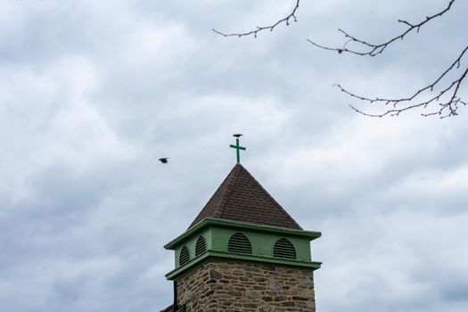 The Tower of a Cobblestone Church With a Cross on Top on a Cloudy Overcast Sky in Suburban Pennsylvania