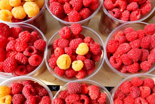 Red and yellow raspberries are collected in plastic cups and sold in street markets, top view.