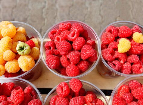 Red and yellow raspberries are collected in plastic cups and sold in street markets, top view, space for text.