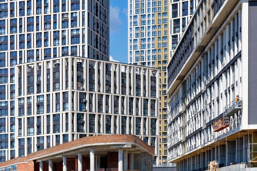 Active construction and facades of new apartment buildings in a residential area of the city block the background of the blue sky.