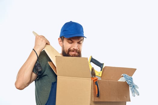 Worker man in uniform with a box in his hands tools delivery service light background. High quality photo