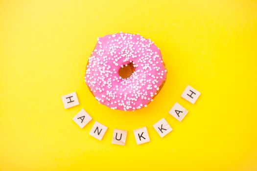 Bright pink delicious donuts on yellow background and inscription from wooden blocks happy hanukkah