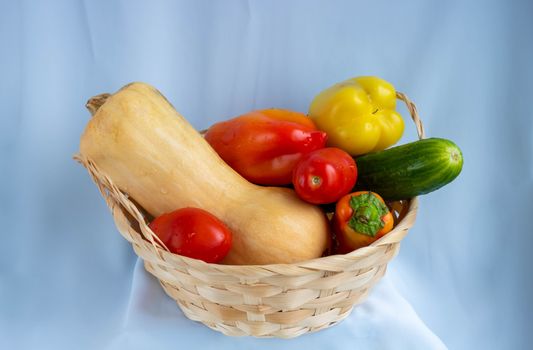 Wicker basket with different vegetables. Pumpkin, pepper, cucumber, tomatoes.Isolated on a blue background.The concept of crop.