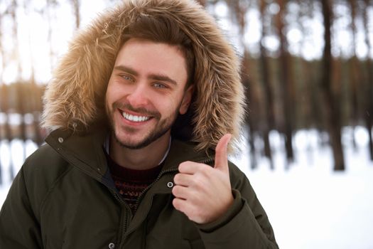 Handsome bearded young caucasian man standing outdoors sweater winter season forest. Attractive stylish european guy walking snowy christmas woodland Season holiday leisure Showing thumbs up gesture