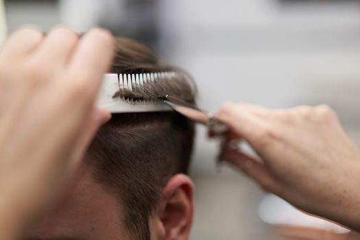 Beautiful caucasian woman hairdresser doing hairstyle to client. Close up portrait female barber with hairdressing tools at work. hair cutting process Hairstyling in modern barbershop. Professional