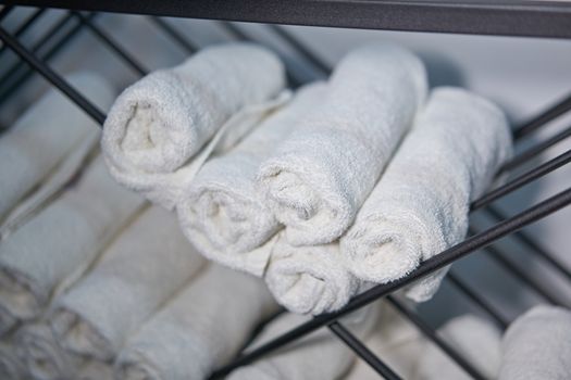 White clean towels rolled up on a roll are stored on shelves in a beauty salon in a barbershop spa. Close up towel storage