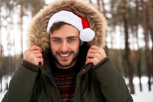 Handsome bearded young caucasian man standing outdoors sweater santa hat winter season forest. Attractive stylish european guy walking snowy christmas woodland Season holiday leisure