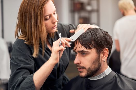 Stylish man sitting barber shop Hairstylist Hairdresser Woman cutting his hair Portrait handsome happy young bearded caucasian guy getting trendy haircut Attractive barber girl working serving client