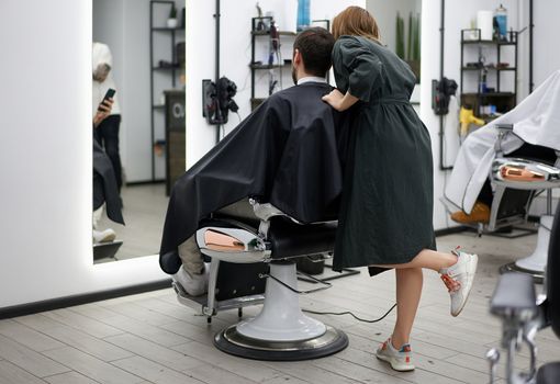 Stylish man sitting barber shop Hairstylist Hairdresser Woman cutting his hair Portrait handsome happy young bearded caucasian guy getting trendy haircut Attractive barber girl working serving client