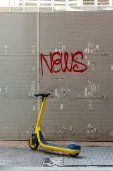 Bright yellow scooter parked in front of a wall with the word "news" written, street photography in an Italian city