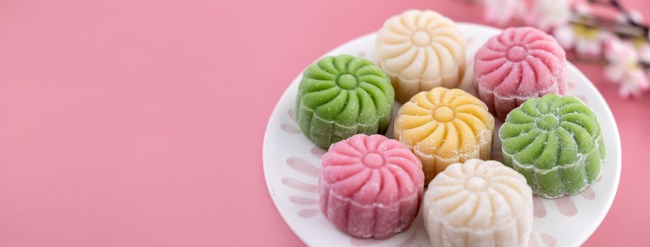 Colorful snow skin moon cake, sweet snowy mooncake, traditional savory dessert for Mid-Autumn Festival on pastel pale pink background, close up, lifestyle.