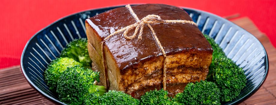 Dong Po Rou (Dongpo pork meat) in a beautiful blue plate with green broccoli vegetable, traditional festive food for Chinese new year cuisine meal, close up.