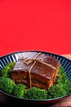 Dong Po Rou (Dongpo pork meat) in a beautiful blue plate with green broccoli vegetable, traditional festive food for Chinese new year cuisine meal, close up.