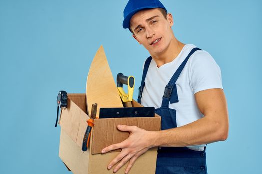 working man in uniform box with tools loader delivery blue background. High quality photo