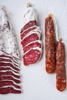Variety of dry cured fuet and chorizosalami sausages, whole and sliced on white surface, top view.