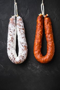 Spanish salami, fuet and chorizo sausages hang from a rack on black background.
