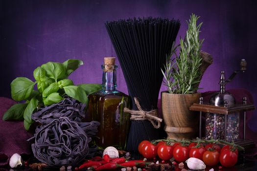 Various pasta and with herbs, spices condiments on black purple background. Cooking concept.