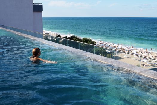 teenage girl swimming in the rooftop pool with sea view.