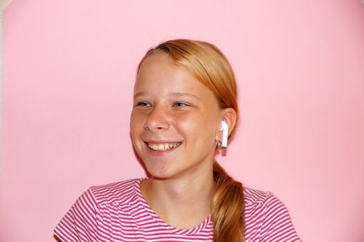 teenage girl listening to music on headphones and smiling, portrait on pink background.