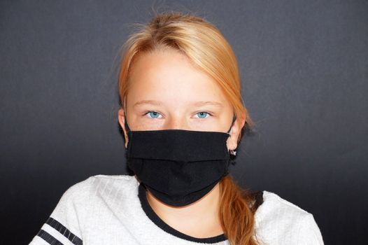 teenage girl in a black medical mask on a black background, portrait.