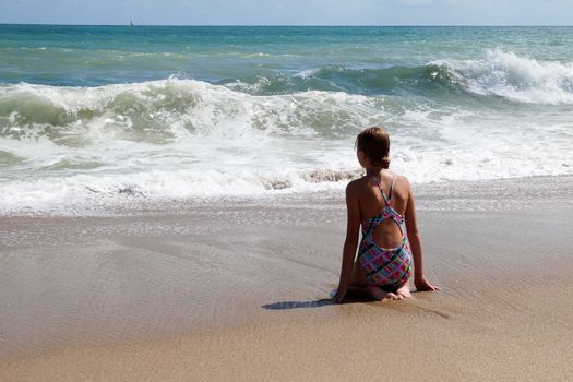 teenage girl sitting alone on the wet sand and looking at the sea.