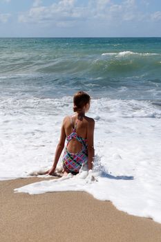 teenage girl sitting in white sea foam and looking at the sea.